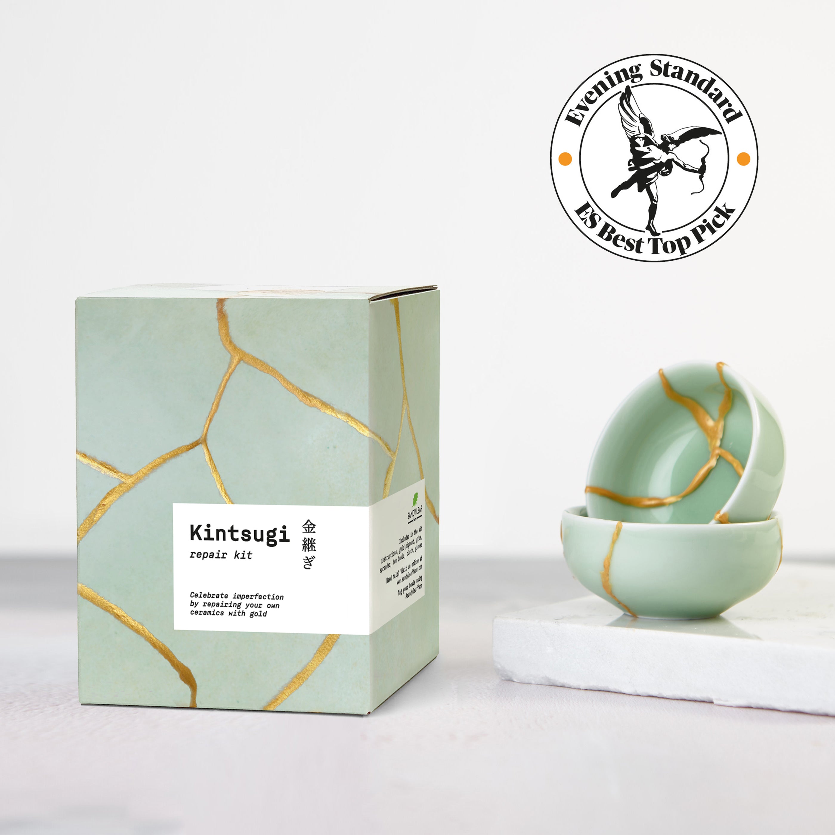 Kintsugi repair kit with gold powder, epoxy and practice bowls laid out on a table