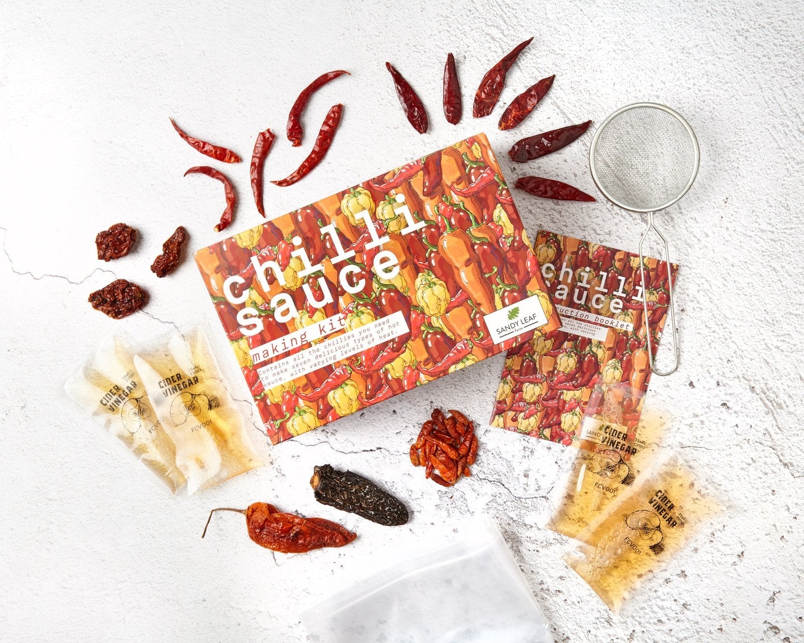 Chilli sauce making kit with six dried chillies, bottles of homemade hot sauce and kraft paper labels
